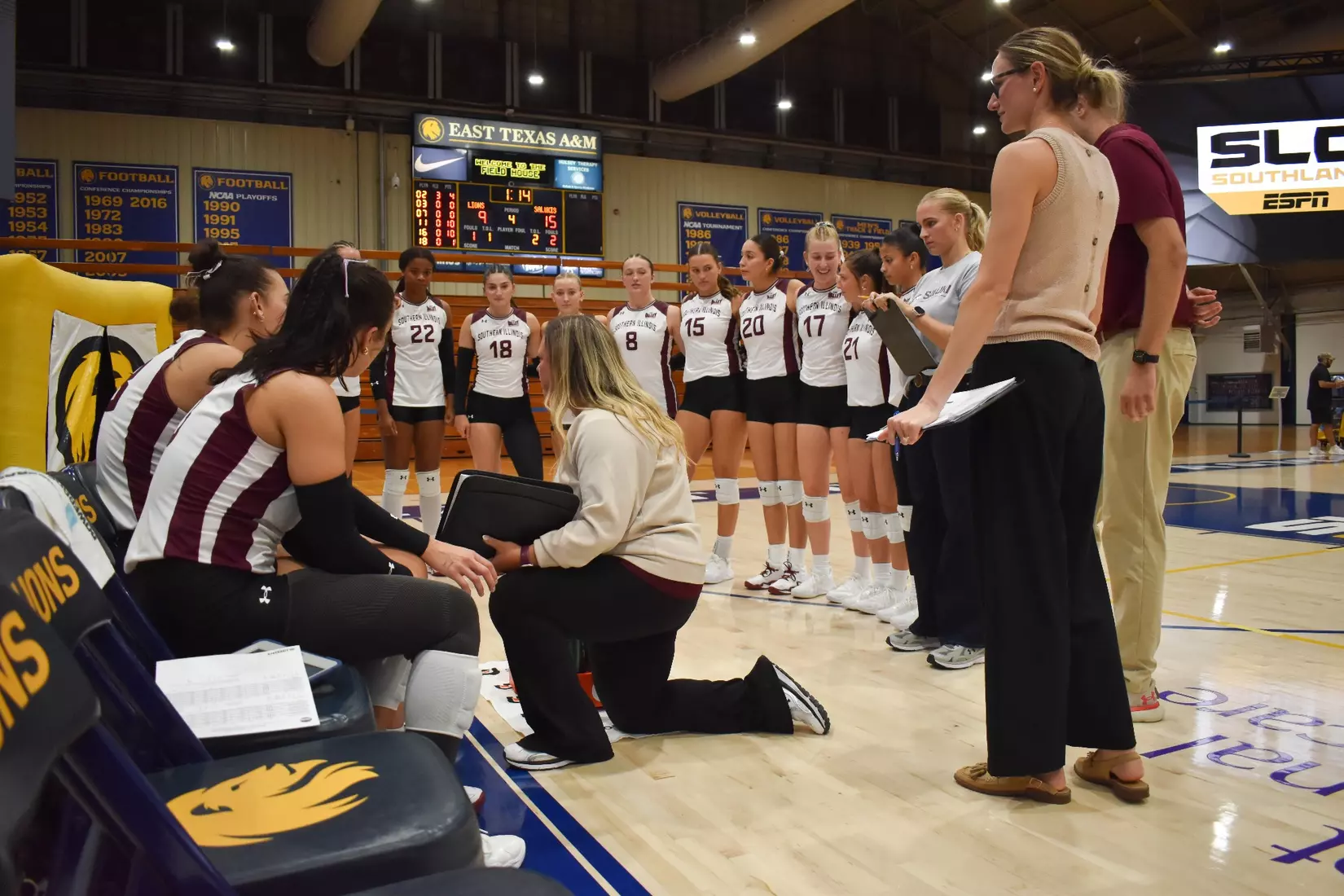 Head Coach Brittany Harry kneels down and talks with her team during a timeout.