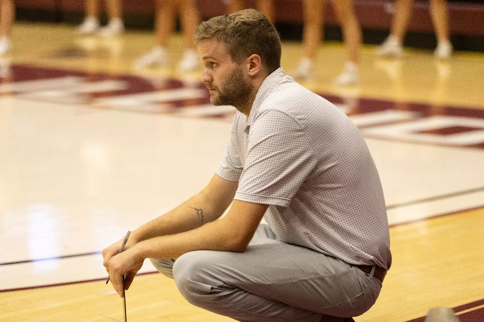 Assistant Coach Chris Yates watches the match in his signature squat.