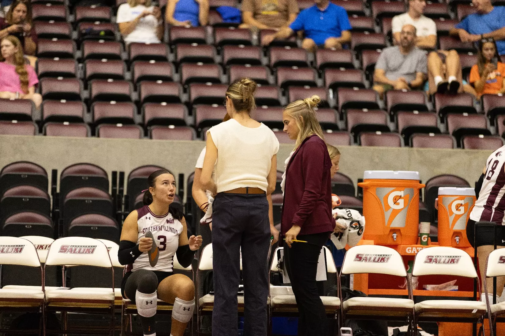 Assistant Coach Bryleigh Buchanan and Graduate Assistant Emma Lade talk with McKenzie Moeller during a timeout.