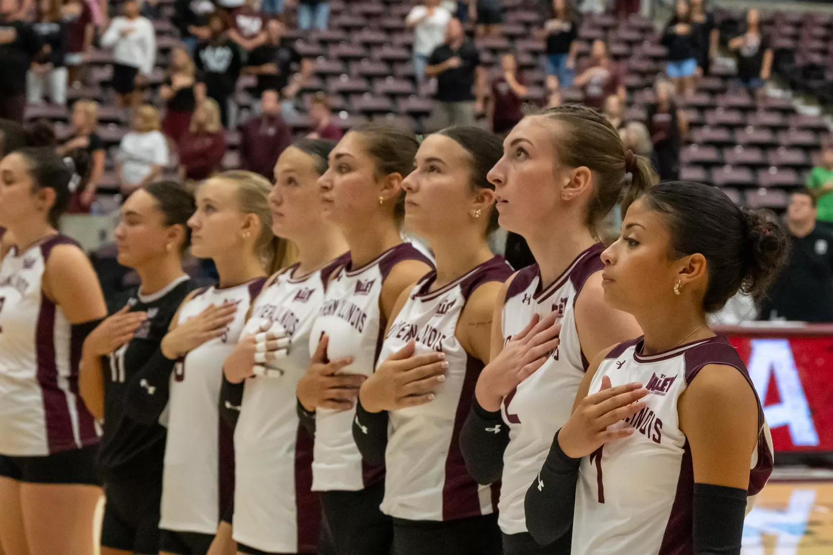 The team stands side-by-side with their hands on their hearts during the national anthem.