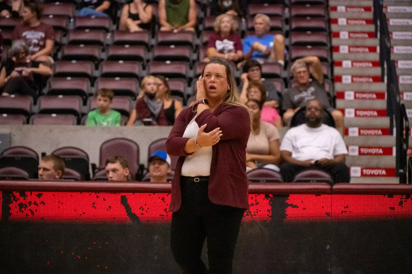 Head Coach Brittany Harry talks to her team as she blocks her mouth with her hand.