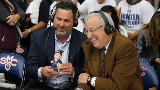 Saint Mary's Director of Athletics and Recreational Sports Mike Matoso (left) poses with an NBC Sports Bay Area broadcaster (right) and a Randy Bennett gnome giveaway item during the Gaels' game versus Dayton on Dec. 19, 2017, at McKeon Pavilion