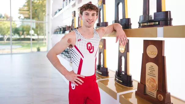 Nathan Roman poses in front of trophies in the lobby of the Sam Viersen Gymnastics Center