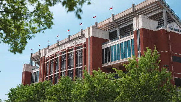 The east side of Oklahoma's Gaylord Family - Oklahoma Memorial Stadium taken through greenery from nearby trees looking from the northeast in April 2025.