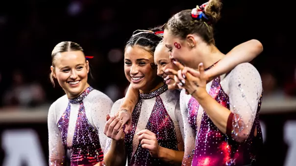 A group of OU gymnasts laughs on the sidelines.