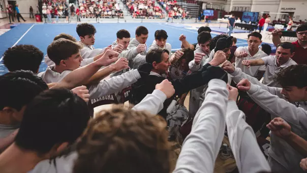 Oklahoma men's gymnastics team huddle before a meet at McCasland Field House with blue floor exercise floor and crowd in background