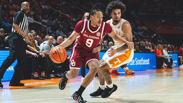 OU's Nigel Pack in crimson uniform dribbles against a Tennessee defender in white uniform at Tennessee's Thompson-Boling Arena on Feb. 18, 2026