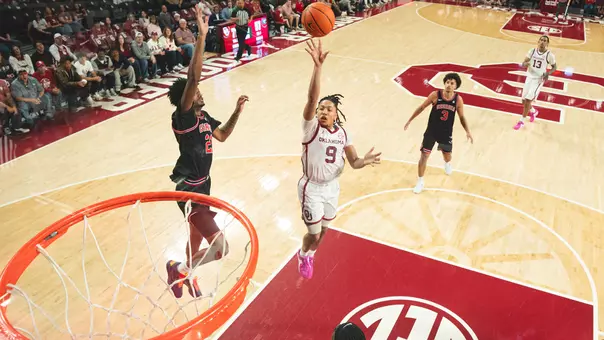 Nijel Pack in white uniform goes up for a layup against a Georgia defender in black uniform at Lloyd Noble Center, photo taken through the backboard