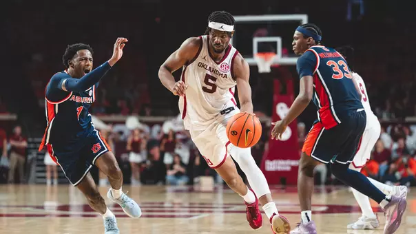 OU's Mohamed Wague in white uniform drives against Auburn defenders in navy uniform at Lloyd Noble Center on Feb. 24, 2026
