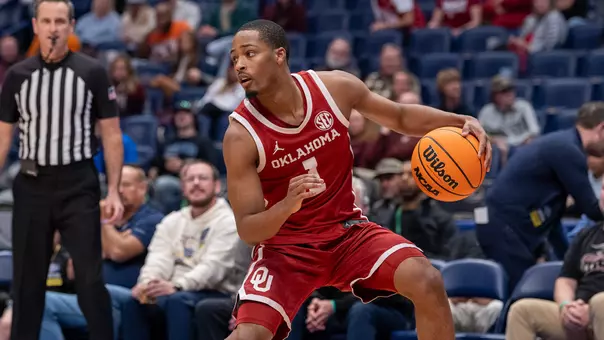 OU's Xzayvier Brown in red uniform dribbles during and SEC Tournament basketball game at Bridgestone Arena in Nashville, Tenn.