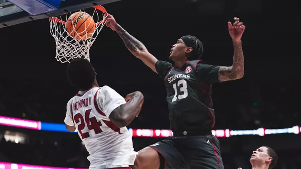 Tae Davis in dark gray uniform dunks over an Arkansas defender in white uniform during the SEC Tournament at Bridgestone Arena in Nashville, Tenn.