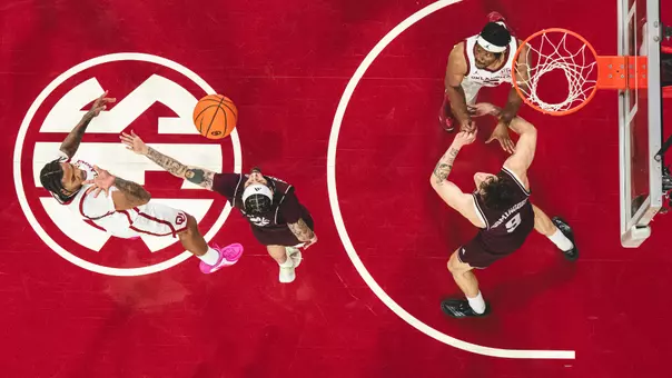 Overhead photo of Tae Davis shooting a jump shot over a defender with Mohamed Wague fighting for position; red-painted lane with SEC logo is background