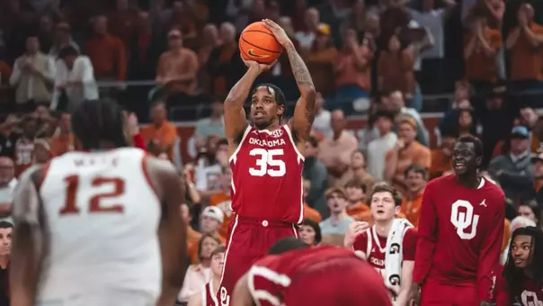 Derrion Reid in red uniform shoots a 3-pointer from the baseline late in overtime of OU's win at Texas (defender in white uniform) in Austin, Texas, on March 7, 2026.