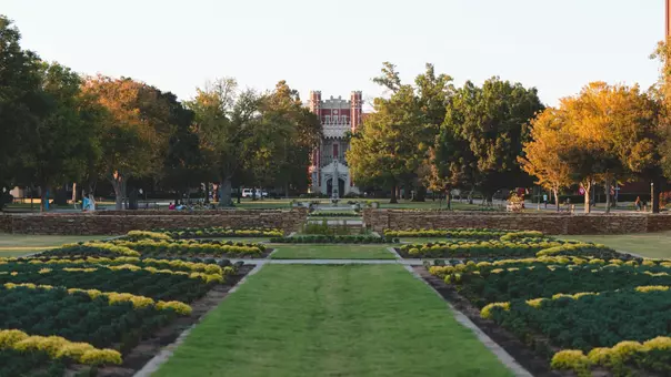 OU South Oval photo with flowering plants, green grass and blue sky and Bizzell Memorial Library in the center distance