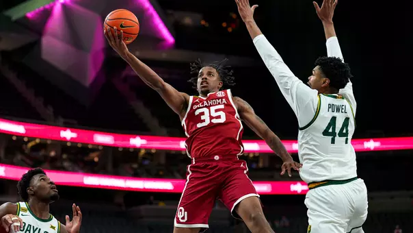 Derrion Reid in red uniform goes up for a layup around a Baylor defender in white uniform at T-Mobile Arena in Las Vegas, Nevada.