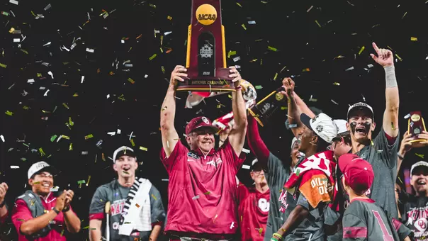 OU head coach Skip Johnson hoists the national championship trophy on the stage surrounded by his players while confetti falls around them on the field at Charles Schwab Field Omaha after winning the 2026 NCAA Division I Baseball National Championship in Omaha, Nebraska.