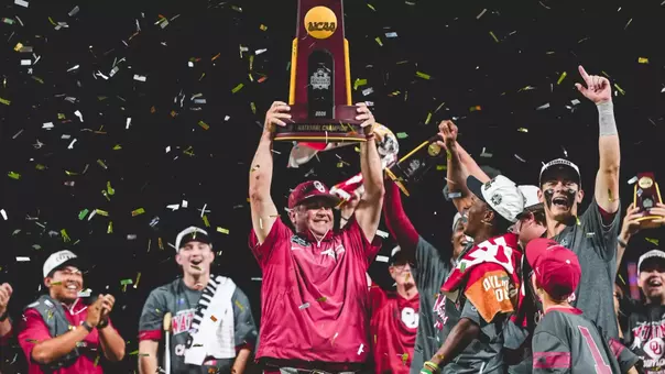 OU head coach Skip Johnson hoists the national championship trophy on the stage surrounded by his players while confetti falls around them on the field at Charles Schwab Field Omaha after winning the 2026 NCAA Division I Baseball National Championship in Omaha, Nebraska.