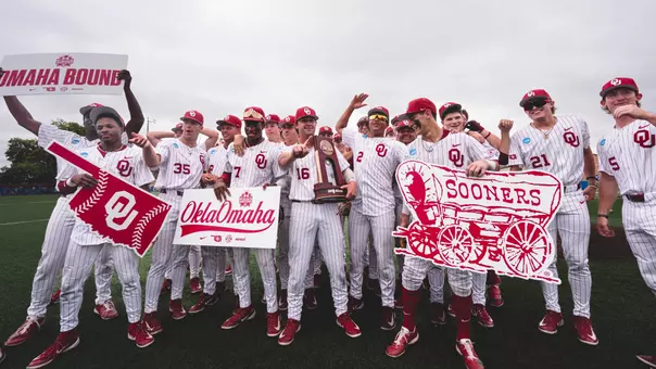 The Oklahoma baseball team celebrates its Lawrence Super Regional Championship after beating Kansas 13-2 Monday afternoon on the field at Hoglund Ballpark in Lawrence, Kansas. Players are holding the NCAA Super Regional champion trophy and signs including an interlocking OU logo sign, the Sooner schooner sign, OklaOmaha sign and an Omaha Bound sign.