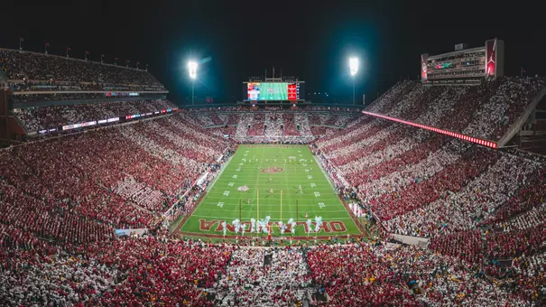 Wide photo of Gaylord Family - Oklahoma Memorial Stadium at night with full crowd