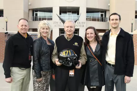 Long-time Southern Miss football radio analyst Vic Purvis (middle) receives a helmet with the number of the broadcasts conducted over his 41-year career. Purvis retired following the UAB contest which concluded the Golden Eagles' 2014 season. Southern Miss Director of Athletics Bill McGillis (far left), along with Purvis' wife, Gaye (second from left), daughter Vicki (far right), and husband Matthew Tubbs join Vic for the recognition of his accomplishments at halftime of the contest.