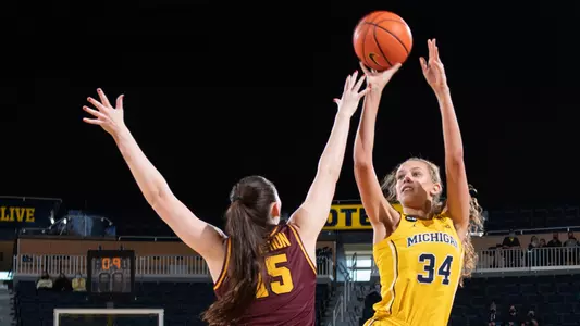 Woman in Michigan uniform takes jumpshot.