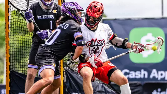 Chaos attackman Bradley Voigt drives against his Waterdogs opponent, cradling his stick left handed. He wears a white shersey while his opponent wears a black Waterdogs shersey.
