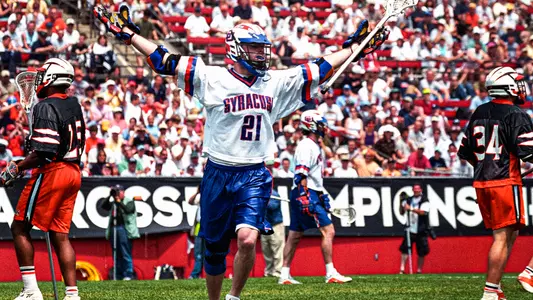 Sean Lindsay, wearing a classic Syracuse porthole jersey, throws his hands up in celebration of a goal in the 2002 NCAA Championship game. Two Princeton players stand on each side of the frame, looking dejected.