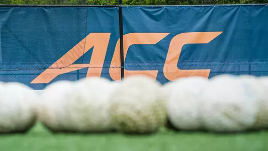 A windscreen with a dark blue background and the ACC logo in Syracuse Orange with a pile of field hockey balls in the foreground.