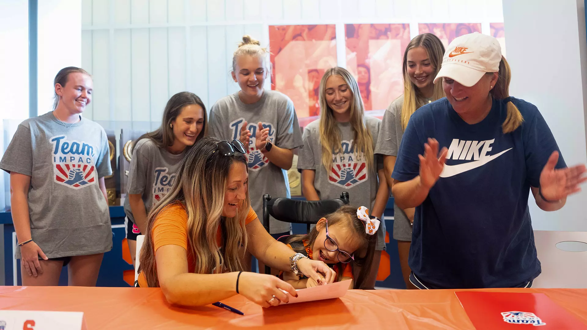 Lilianna signs her letter, making her an official member of the Syracuse women's soccer program, while Coach Nicky Thrasher Adams looks on.