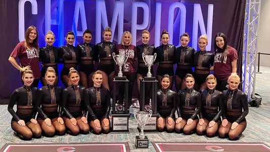 The dance team poses with two trophies in front of a champion banner in Orlando in April 2021.