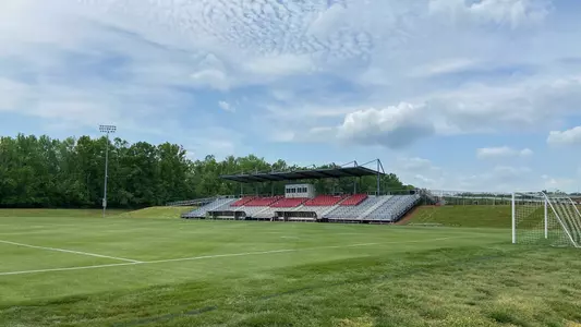 Macpherson Stadium in Greensboro, North Carolina on a pleasant April afternoon. The stadium features a solitary set of stands under a canopied roof. A small press box caps off the center of the seven seating sections. The sky is a hypnotic blue with a blanket of wispy white clouds.