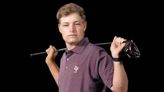 Jake Maggert in a portrait shoot in front of a stark black background with golf club Bo Jacksoned behind his neck.