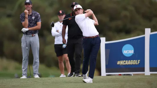 Daniel Rodrigues holds the back swing on a titanic drive while wearing an white polo with maroon Aggies script, blue pants and a white cap with a maroon Block T