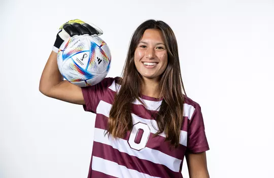 Maysen Veronda posing, flexing with a soccer ball lodged between her bicep and forearm in front of a stark white back drop.