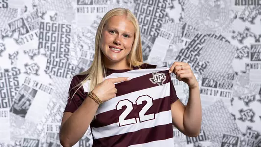 Margo Matula pops the Texas A&M logo with her left hand and points at emphatically with her right hand in a classy content day portrait shoot.