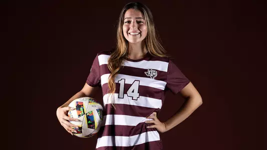 Mia Scranton poses in front of a black background, holding a soccer ball against her right hip