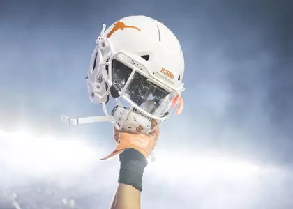 Football player raising his helmet with a blue sky.