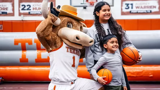 UT's official costume mascot, Hook 'Em, posing and doing a hook 'em hand sign alongside two children inside Denton Cooley Pavilion during the Longhorns Kids Court