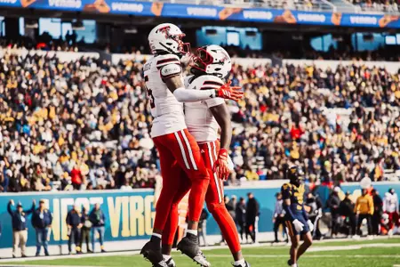 Two Texas Tech players in white jerseys and red pants celebrate in the end zone, chest bumping after a scoring play.