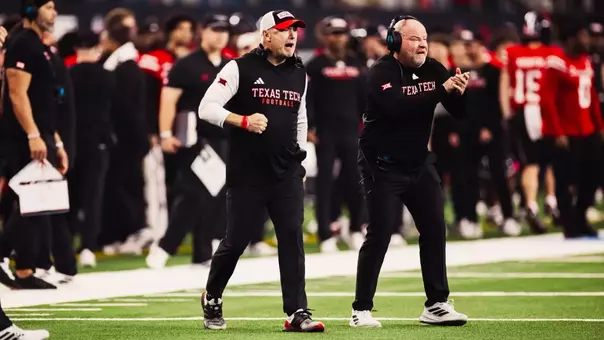 Texas Tech head coach Joey McGuire and an assistant coach celebrate on the sideline during a football game, with players and staff blurred in the background.