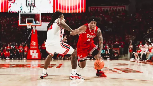Texas Tech forward JT Toppin, in a red No. 15 jersey, dribbles past a Houston defender on the perimeter during a road game.