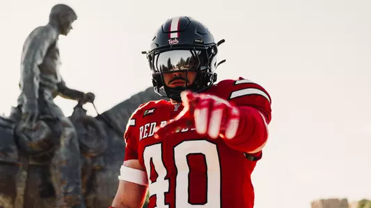Wesley Smith points at the camera in front of the Will Rogers statue in a black helmet and red jersey for the Arizona State uniform reveal on TexasTech+.