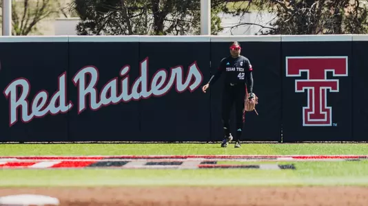 Mihyia Davis standing in center field infront of the outfield wall padding that says Red Raiders