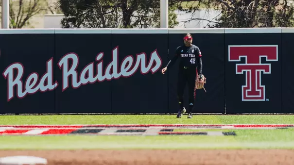 Mihyia Davis standing in center field infront of the outfield wall padding that says Red Raiders