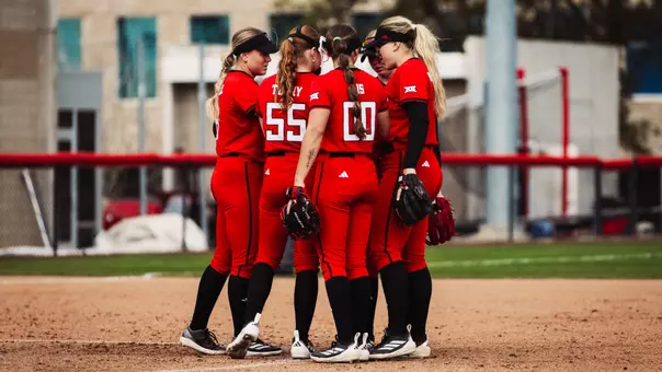 Texas tech's softball team huddled together at the pitchers circle in red jerseys