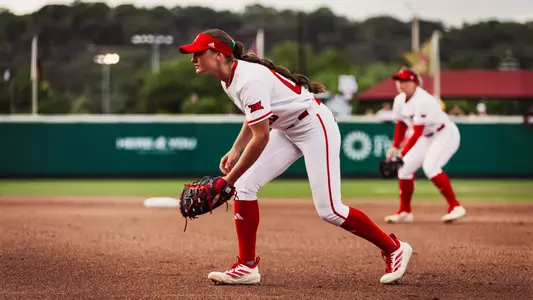 Jackie Lis crouching in defensive position at first base in an all-white jersey