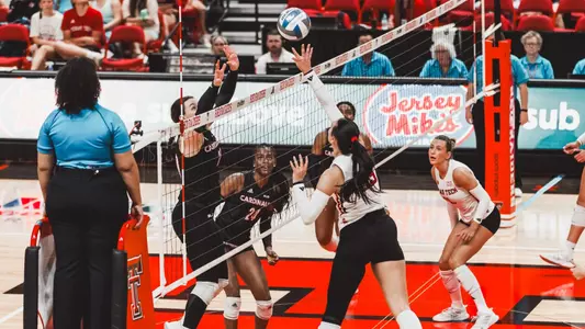 Ashlyn Bellamy tipping a ball over the net against an Incarnate Word defender with Tatum Johnson looking on in the background