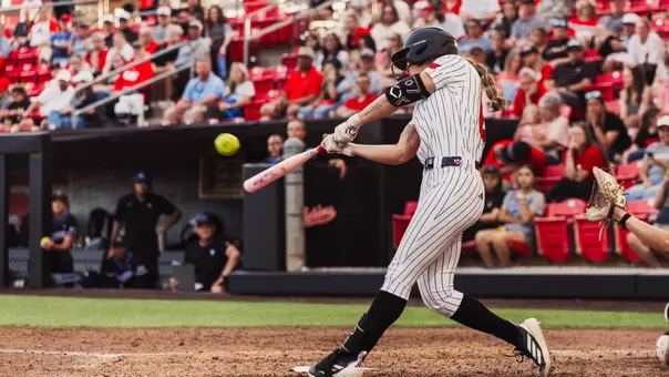 Jackie Lis hitting a softball in a white pinstripe jersey at Tracy Sellers Field