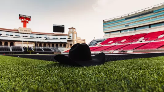 Photo of a black cowboy hat sitting on the Jones AT&T Stadium turf with the Double T Scoreboard in the background.