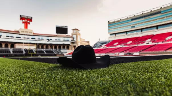 Photo of a black cowboy hat sitting on the Jones AT&T Stadium turf with the Double T Scoreboard in the background.